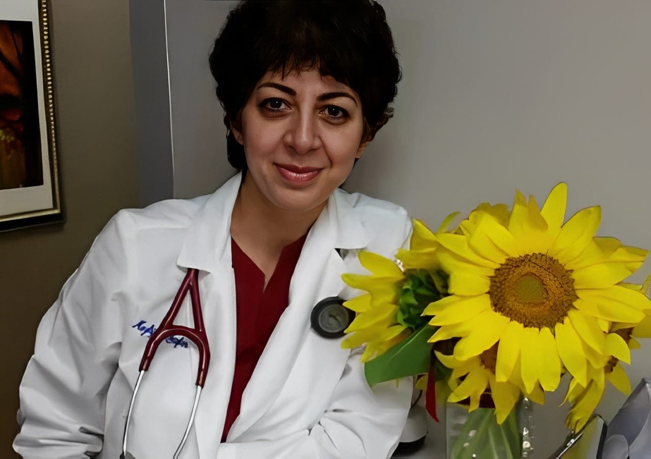 A woman in white lab coat holding a yellow flower.