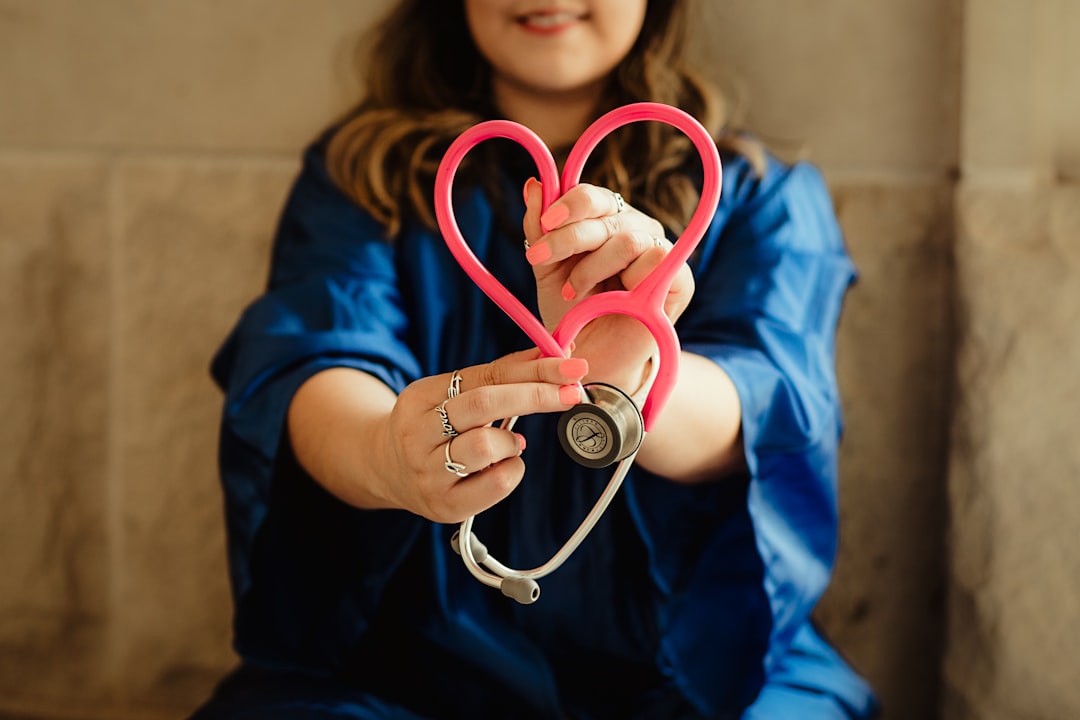 Healthcare professional forming a heart shape with a pink stethoscope